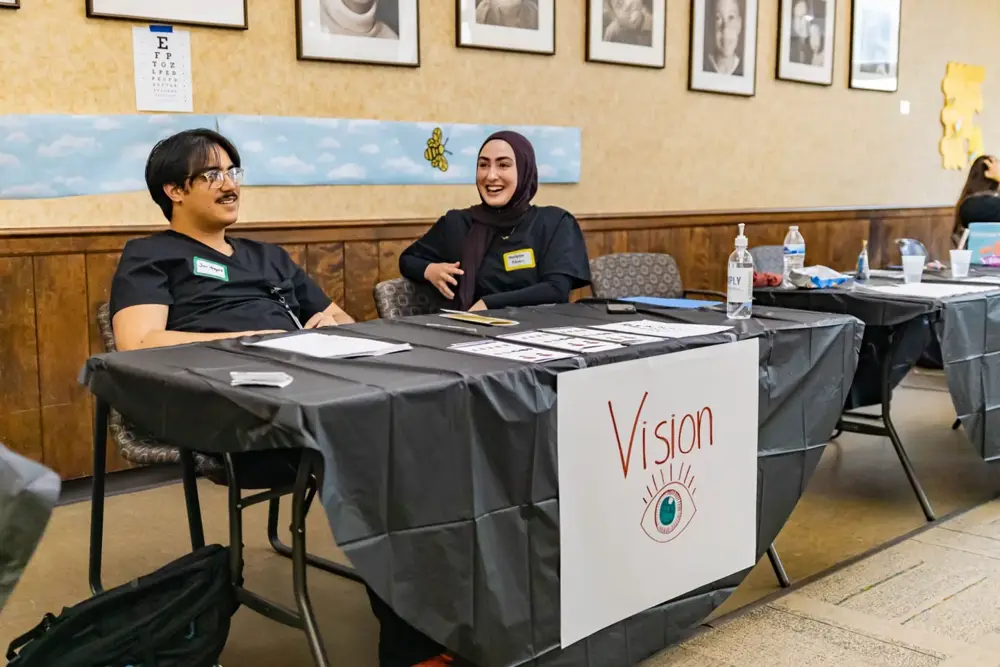 Smiling conversation at the vision exhibit table during the Neighborhood House health fair.