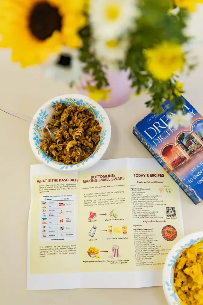 A nutrition guide with recipes and food substitutions beside a prepared meal, sunflowers, and a Dream Dictionary from the Library of Consciousness