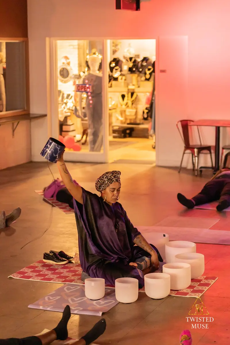 A seated sound practitioner holding a bowl above a circle of singing bowls at Sherman Phoenix